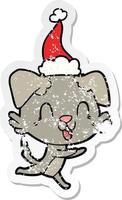 laughing distressed sticker cartoon of a dog wearing santa hat vector