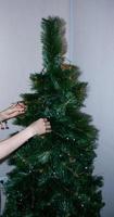 una mano femenina decora el árbol de navidad con juguetes de navidad y año nuevo. mano de mujer decora el árbol de navidad con guirnaldas. foto
