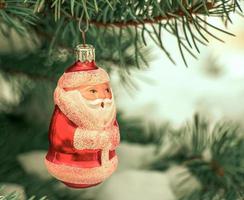 Christmas toy Santa Claus hangs on a snow-covered branch of a Christmas tree on a festive background of white snow bokeh with copy space. photo