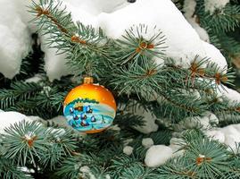 Christmas ball hanging on a snow-covered branch of a Christmas tree on a festive background of white snow and snowy bokeh with copy space. photo