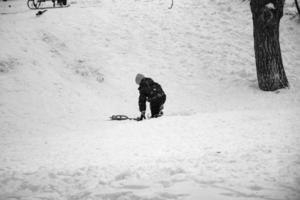 Little boy sledding downhill in winter. The boy falls into the snow. Outdoor play for children. Children's sledges in a snow-covered park. photo