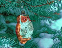 el búho de juguete de navidad cuelga de una rama cubierta de nieve de un árbol de navidad sobre un fondo festivo de nieve blanca con espacio para copiar. foto