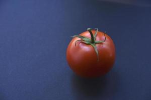 Red fresh tomato on a black background. One tomato fruit close-up. photo