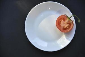 Ripe beautiful tomato fruit on a white plate top view. Delicious tomatoes still life. photo