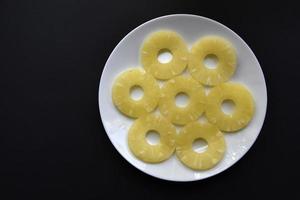 deliciosos anillos de piña fresca en un plato sobre un fondo negro. delicioso desayuno de anillos de piña. foto