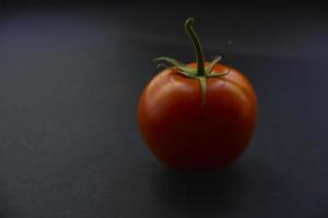 tomate fresco rojo sobre un fondo negro. primer plano de una fruta de tomate. foto