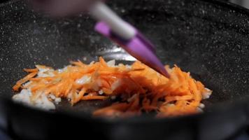 le chef cuisine un ragoût d'oignons blancs et de carottes pour le plat principal dans une poêle sur une cuisinière à gaz, en remuant pour l'empêcher de brûler. video