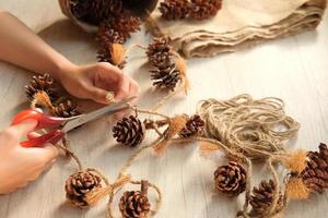 Part of a woman's hands making wall hangings from pine cones and jute rope photo