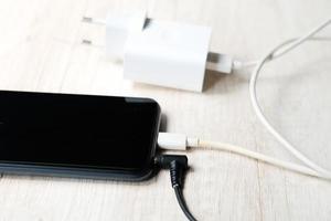 teléfono inteligente moderno enchufado en los cables de alimentación y audio en la mesa foto