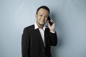 Portrait of an Asian businessman wearing a black suit smiling while talking on the phone photo