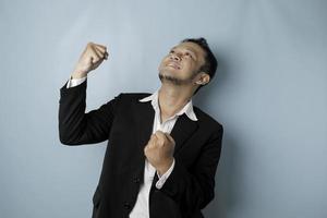 A young Asian man with a happy successful expression wearing suit isolated by blue background photo