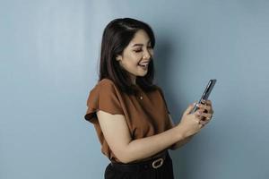 A portrait of a happy Asian woman is smiling and holding his smartphone wearing brown shirt photo