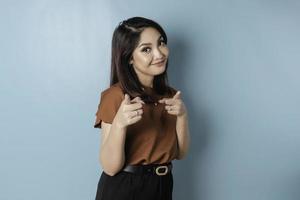 Young beautiful Asian girl standing over isolated blue background pointing fingers to camera with happy and funny face. Good energy and vibes. photo