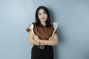 Excited Asian woman holding cooking ware and smiling, isolated by blue background photo