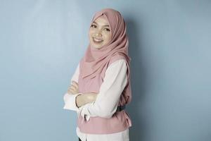 Portrait of a confident smiling Asian Muslim woman standing with arms folded and looking at the camera isolated over blue background photo