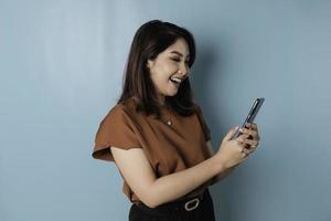 A portrait of a happy Asian woman is smiling and holding his smartphone wearing brown shirt photo