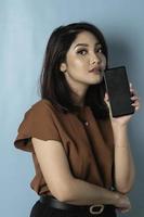 A portrait of young Asian woman in brown shirt feeling serious and focus with holding smartphone in hand. photo