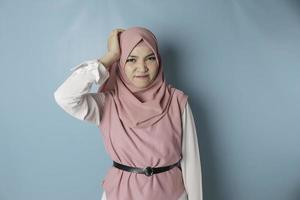 An Asian Muslim girl with a headache holds her head. Sullen young woman on a blue background copy space photo