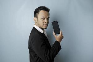 A young Asian businessman in a black suit feels serious and focus holding a smartphone and showing the copy space on its screen in hand. photo