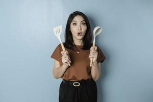 Excited Asian woman holding cooking ware and smiling, isolated by blue background photo