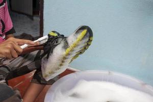 Washing the dirty shoes or sneakers in bubble-filled basin. photo