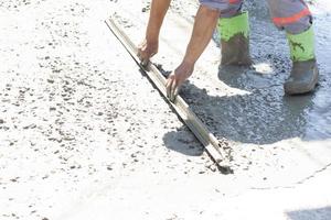 Construction workers are working by leveling the concrete floor smooth in the heat of the sun. photo