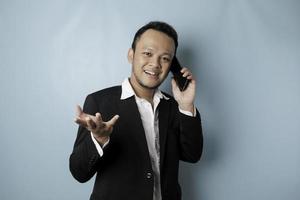 Portrait of an Asian businessman wearing a black suit smiling while talking on the phone photo