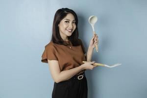 Excited Asian woman holding cooking ware and smiling, isolated by blue background photo