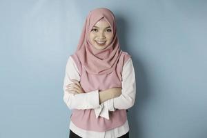 retrato de una mujer musulmana asiática sonriente y confiada de pie con los brazos cruzados y mirando la cámara aislada sobre fondo azul foto