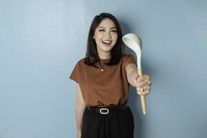 Excited Asian woman holding cooking ware and smiling, isolated by blue background photo