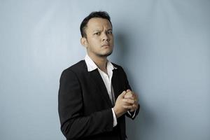 A portrait of a young Asian businessman looks angry and holding his fist ready to punch, isolated by blue background photo