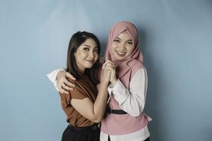 portrait of two girls smiling and hold each other hand isolated on blue background photo