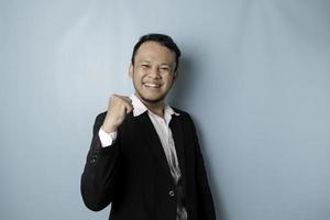A young Asian man with a happy successful expression wearing suit isolated by blue background photo