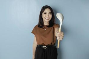 Excited Asian woman holding cooking ware and smiling, isolated by blue background photo