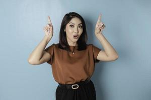 Shocked Asian woman wearing pointing at the copy space upside her, isolated by blue background photo