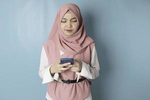 Young Asian Muslim woman in pink hijab feeling serious and focus with holding smartphone in hand. photo