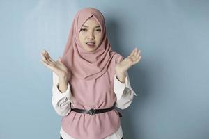 Surprised Asian Muslim woman wearing pink hijab isolated by blue background photo