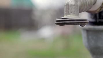 waterkraan op de achtergrond van de natuur. het openen of sluiten van een kraan om water te besparen duidt op een probleem met watertekort. rustieke fontein met daglicht. selectieve aandacht met onscherpe achtergrond. video