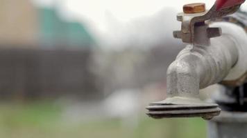 waterkraan op de achtergrond van de natuur. het openen of sluiten van een kraan om water te besparen duidt op een probleem met watertekort. rustieke fontein met daglicht. selectieve aandacht met onscherpe achtergrond. video