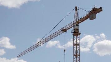 un' Lavorando costruzione Torre gru contro un' nuvoloso cielo su un' soleggiato giorno. il concetto di urbano sviluppo e costruzione. industriale sfondo. gru ingegneria, costruzione industria attrezzo. video