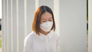 une femme couvre un masque tout en portant des écouteurs sous un bâtiment. video