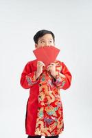 Little Asian boy wearing red traditional Vietnamese suit and holding many of red envelope with smiling face isolated on white background photo