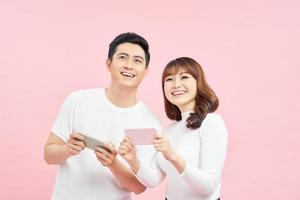 Image of excited couple man and woman smiling while both using mobile phones isolated over pink background photo