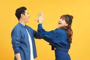 Image of friendly young people man and woman in basic clothing laughing and giving high five isolated over yellow background photo