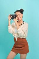 Traveler and photographer. Studio portrait of pretty young girl holding photocamera. Blue blackground. photo