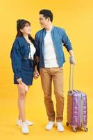 Traveler asian couple with backpack and suitcase standing isolated over yellow background photo