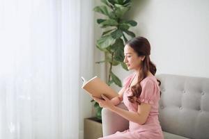 concepto de ocio, literatura y personas - mujer asiática sonriente leyendo un libro en casa foto