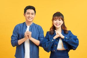 Young couple posing in a yellow background clasping hands at camera in congratulations gesture. photo