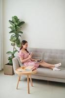 Beautiful young Asian woman using laptop while sitting at living room and drinking coffee photo