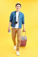 feliz turista masculino con bolsa de viaje y cámara lista para el viaje, aislado en amarillo foto